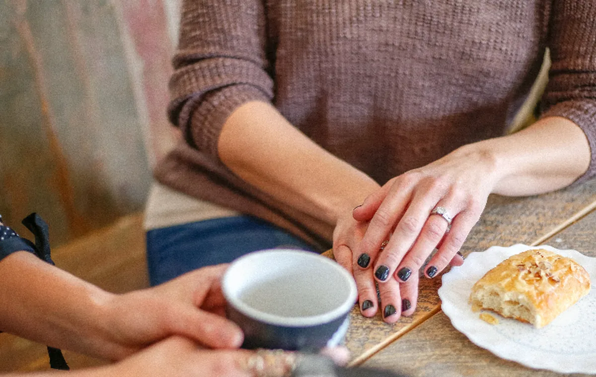 Two people talking across a café table, hands resting beside a coffee cup.