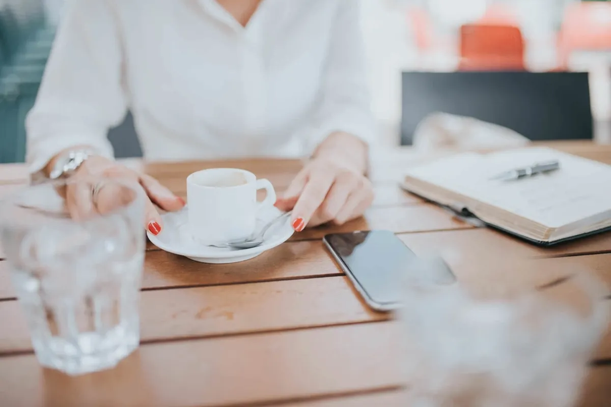 A phone lying face down on a café table next to a notebook and a cup of coffee.